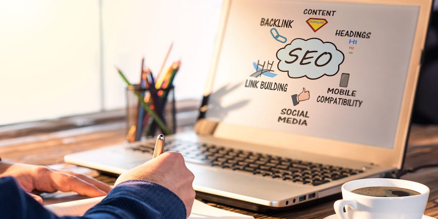 Backlink et leviers SEO sur un écran Ordinateur portable affichant un schéma SEO (backlink, contenu, titres, réseaux sociaux), main prenant des notes