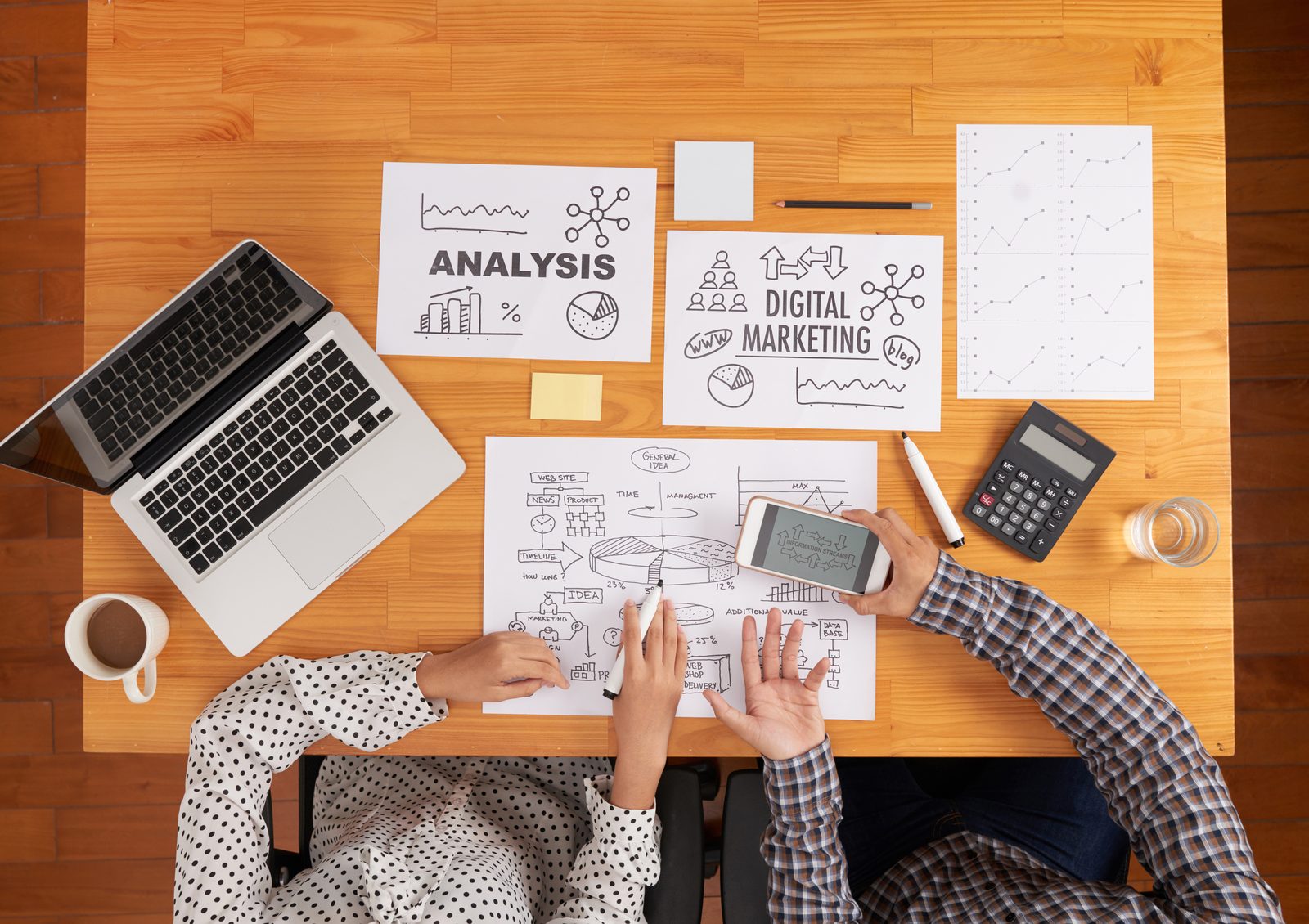 Agence de communication ou freelance Deux personnes qui comparent des schémas de marketing digital sur un bureau : agence de communication ou freelance