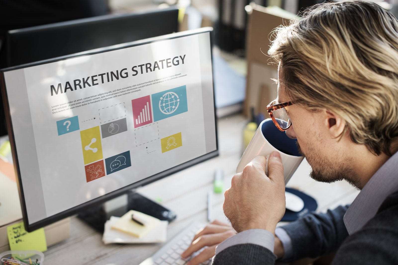 Homme à lunettes qui boit un café devant un écran de stratégie marketing, pour bâtir son plan de communication